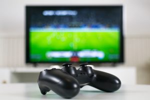 Game Controller Against Blurred Football Match on Screen