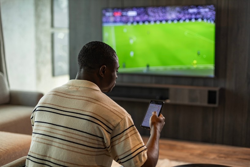Man Checking Phone Whilst Watching Football on TV
